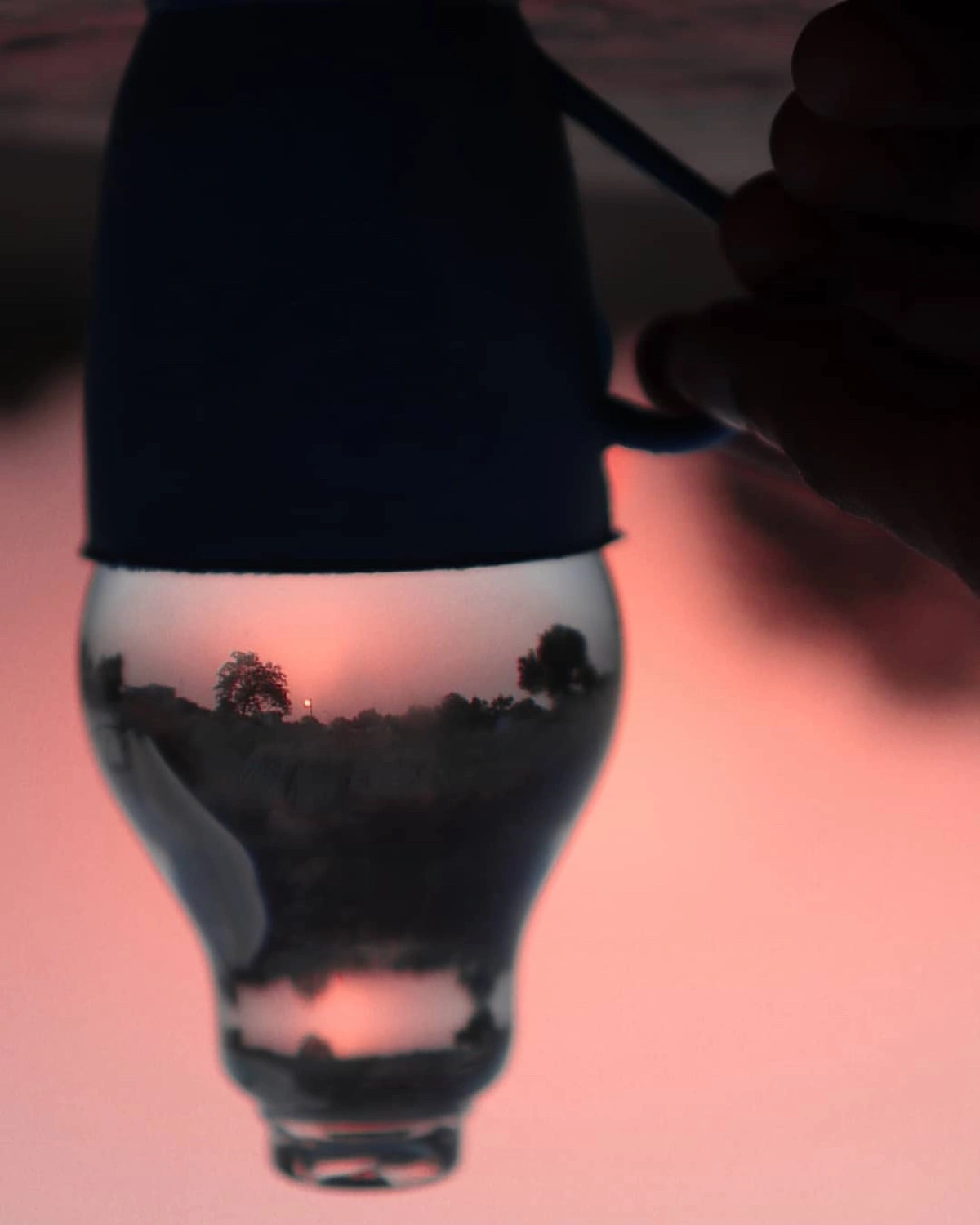 A sunset landscape refracted upside down inside a glass on a pink surface